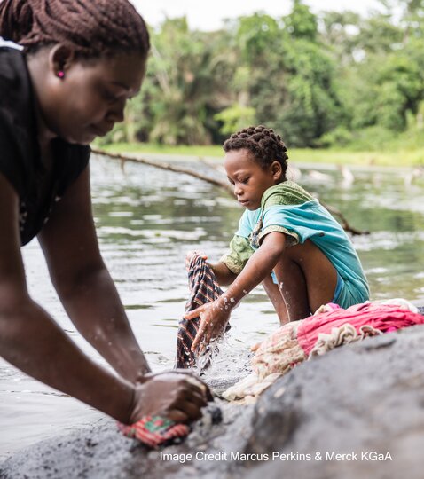 A woman and a girl washing clothes by the side of a lake. Credit Marcus Perkins/Merck KGaA