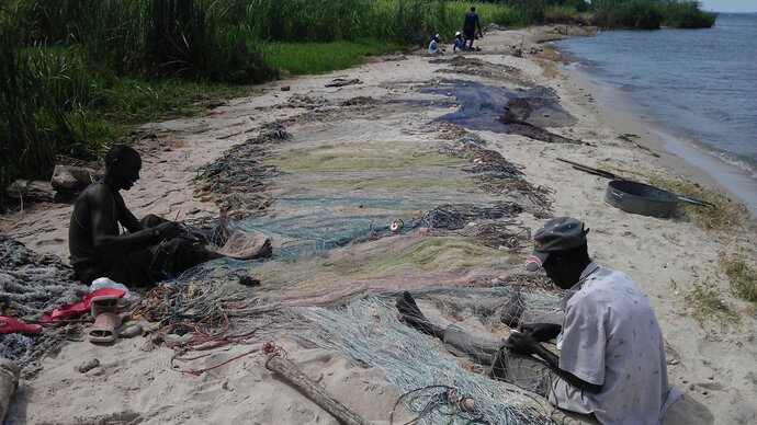 Fishermen mending nets next to a lake. Image copyright Anouk Gouvras