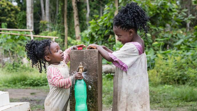 Two children filling a bottle of water from a tap