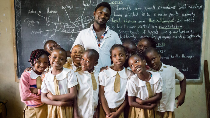 Smiling, a teacher and his pupils stand infront of a blackboard which they have been studying.