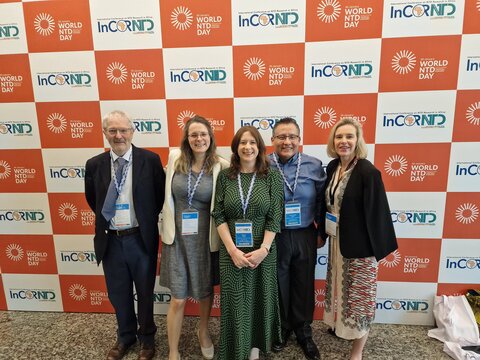 A group of people standing in front of a wall with the InCORNTD and World NTD Day logos. Left to right - David Rollinson, Anouk Gouvras, Fiona Fleming, Carlos Torres Vitolas, Wendy Harrison.