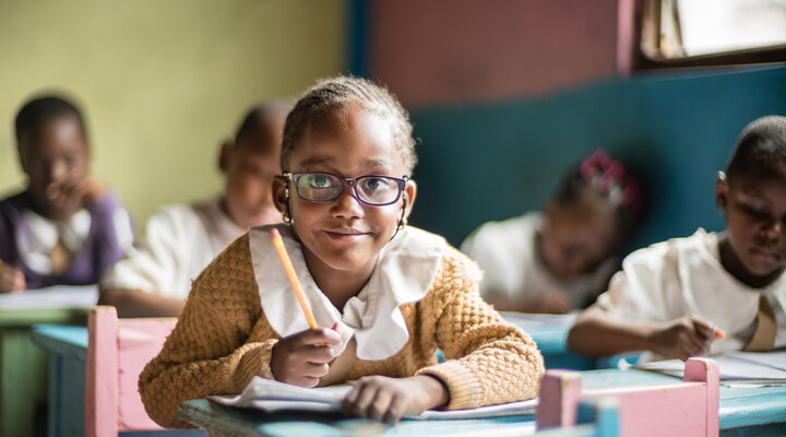 Little girl looks up from her desk at school