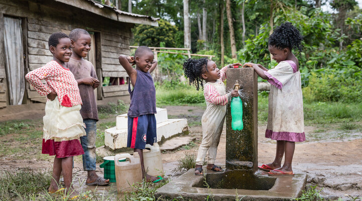 Five children of different ages collecting water into bottles from a tapped water pump